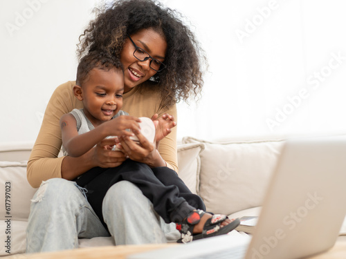 Multiethnic woman sits in living room have fun relaxing at home with her little son. Cheerful biracial child happy smile bonding with his curly hair mother. Enjoyment and love in childhood lifestyle