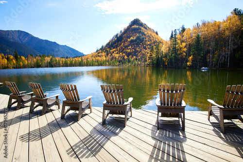 Beautiful autumn landscape. Wooden deck chairs on the lake shore. Outdoor recreation.