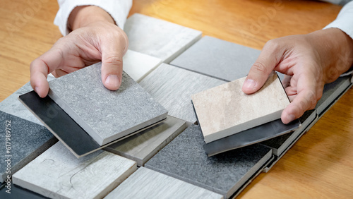 Architect hand choosing sample of stone material or tile texture collection on the table in studio. Designer working for interior architecture and furniture design project.
