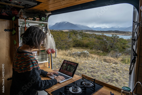 Elderly woman works on her laptop inside a motorhome in front of a scenic landscape in the area of Lake Roca, Santa Cruz, Argentine Patagonia.