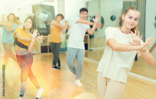 Smiling teenage girl dancer practicing active vigorous dance with group in modern studio.