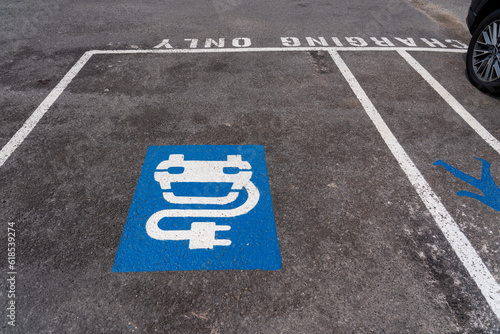 A white vehicle and plug sign in a blue rectangle on an asphalt floor to show parking and charging services for electric vehicles in a public car park
