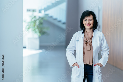 Portrait of positive female doctor psychologist in lab white coat in lobby of in modern hospital clinic office. Medicine, profession and healthcare concept.