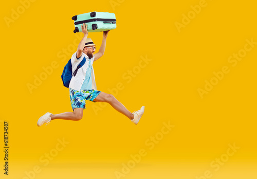 Funny tourist man in summer shirt and shorts, with suitcase and backpack running and jumping isolated on orange yellow background. Summer, holiday, vacation, traveling, hurrying, rush concept
