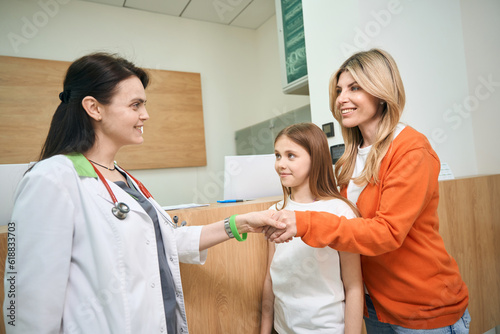 Mother of little patient shaking hand to female pediatrician