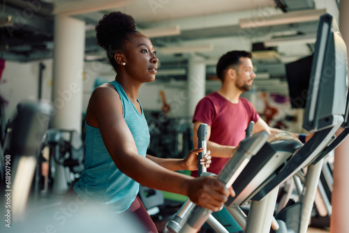 Young black sportswoman using elliptical trainer while exercising in gym.