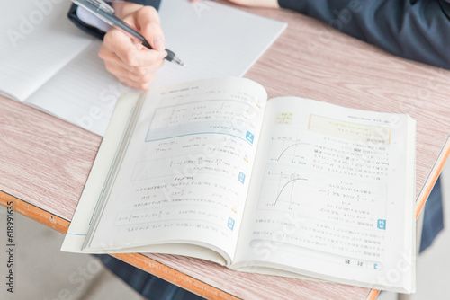 学校の教室で数学の教科書・参考書を見ながら勉強する女子高校生・中学生の生徒 