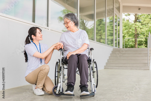 病院・介護施設で散歩しながら話す車椅子に乗った高齢者と介護士（ヘルパー・理学療法士） 