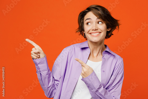 Young woman wear purple shirt white t-shirt casual clothes point index finger aside indicate on workspace area copy space mock up isolated on plain orange background studio portrait Lifestyle concept