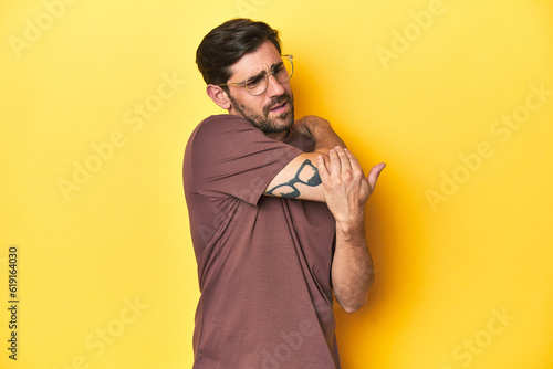 Man stretching arm on a yellow studio background.