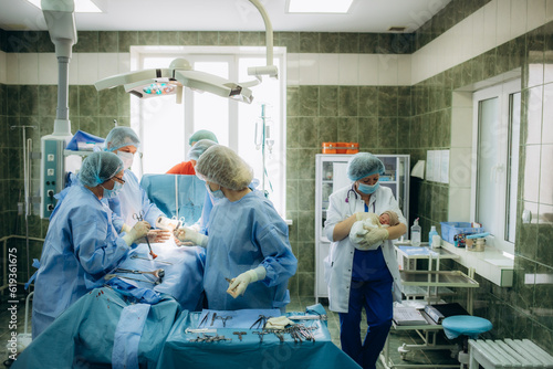 surgeons perfoming surgery operation of abdominal cesarean section during child delivery birth at clinic operating room.