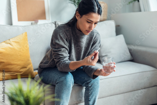 Depressed sad woman taking pills while sitting on couch at home.