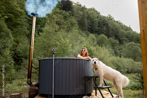 Woman bathing in outdoor hot tub while resting with her cute dog at house in mountains. Concept of recreation and spending leisure time with pets on nature
