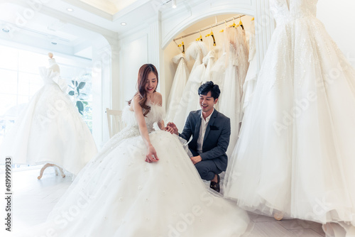 Asian beautiful bride trying on wedding gown with her fiance in studio. 