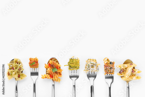 Forks and spoons with various tasty pasta on white background, flat lay. Space for text