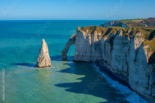 Chalk or limestone cliffs and natural arches and a pointed formation called L'Aiguille along the English Channel in Étretat, Normandy, France. Seascape on a clear day.
