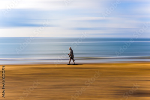 Lonely walk. A man walking alone along the sea shore on a sandy beach. The background has a path blur.