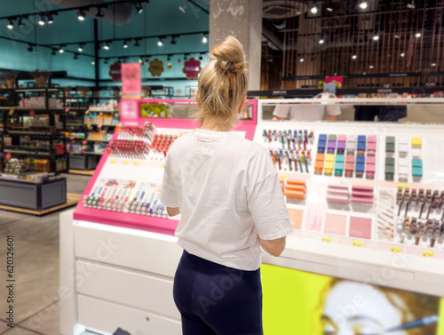 Woman buying make up at cosmetics section in store. choosing cosmetics, perfumes, creams and shampoos, Using tester.