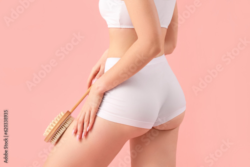 Young woman massaging her leg with anti-cellulite brush on pink background, closeup