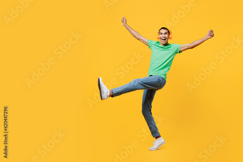 Full body happy young man of African American ethnicity he wears casual clothes green t-shirt hat listen to music in headphones isolated on plain yellow background studio portrait. Lifestyle concept.
