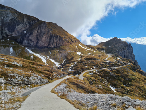 Alpine road over meadows under rocky peaks