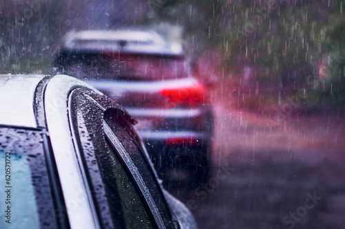 Heavy rain falls on the roof of a car during a thunderstorm. Red brake light in the dark. The concept of auto insurance and natural disasters. Driving on cloudy rainy days. Selective focus.