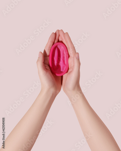 Female hands with reusable menstrual disc on pink background