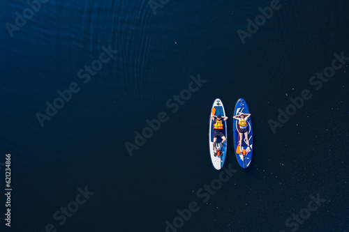 Concept Summer active sport on water. Funny man and woman floats on supboard on lake, top view from drone