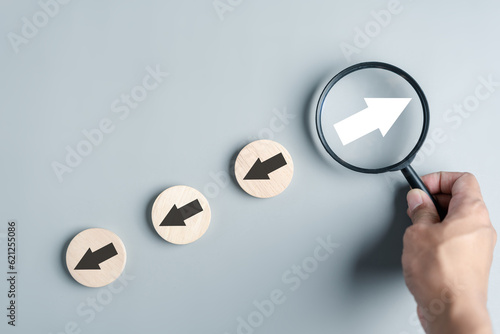 Hand holding magnifier focus to White arrow and different direction facing opposite direction with black arrow for business disruption and technology transformation and different thinking idea