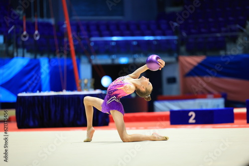 girl gymnast performs an exercise with a ball