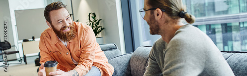 smiling bearded man with takeaway drink talking to entrepreneur on blurred foreground, discussing startup project in lounge of contemporary coworking office, business collaboration, banner