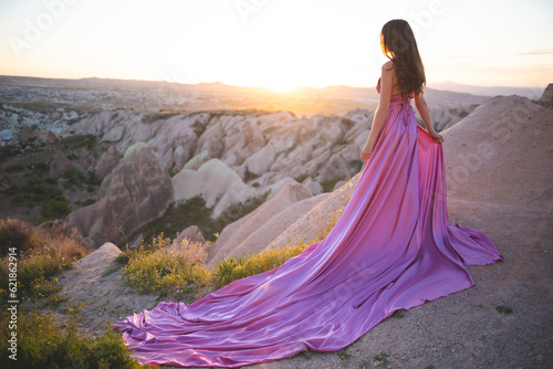 a beautiful girl in a long pink dress poses at sunset in the mountains of Cappadocia