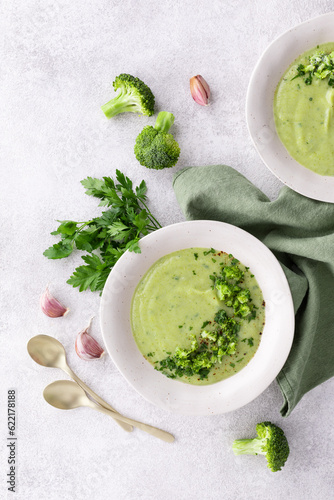Homemade broccoli cream soup with fresh green parsley in white bowl on stone table top view. Healthy vegan dish.