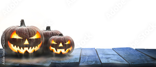 Three lit Jack-o-Lantern, halloween pumpkin lanterns on a wooden product display table with an isolated transparent background.