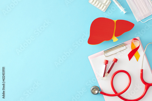 Prevention viral hepatitis concept. Top view of clipboard, liver, awareness ribbon, stethoscope, medical mask, syringe, pills, blood samples on pastel blue background with space for message