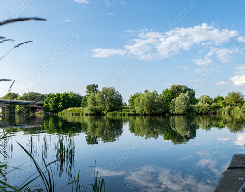 Panorama rzeki Odry w tle most lekko pochmurna pogoda, błękit nieba zieleń przy brzegu, pora letnia, Odra w odcinku województwa Opolskiego 