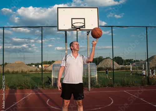Mężczyzna kręcący piłkę do koszykówki na palcu na boisku na świeżym powietrzu, w słoneczny dzień.