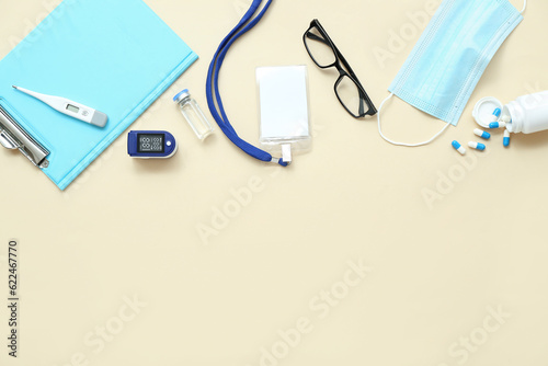 Badge, pulse oximeter, goggles, pills, clipboard and mask on beige background