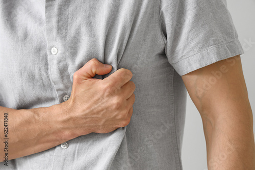 Young man having heart attack on light background, closeup