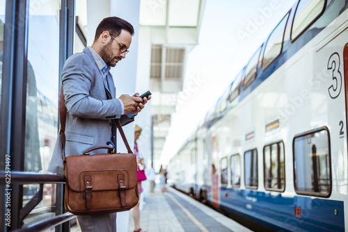 Handsome young man on business trip walking with his luggage and talking on cellphone at train station. Travelling businessman making phone call. Photo of a smiling businessman at train station