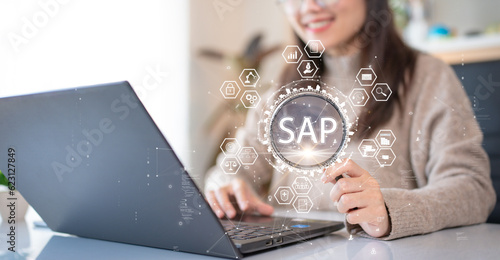 System Applications and Product (SAP). Program helps manage business to access information quickly accurately. Woman using laptop holding magnifying glass with SAP text inside. An icon on background.
