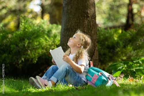School girl listening book in park. Concept of distance learning.