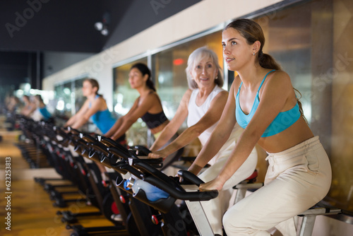 Young sporty woman doing cardio workout out in female group, training on exercise bike