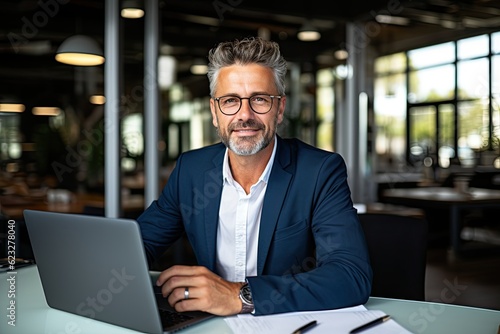 Smiling mature adult business man executive sitting at desk using laptop. Happy busy professional mid aged businessman ceo manager working on computer corporate technology in office