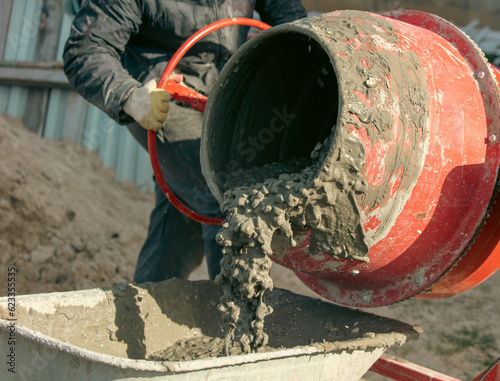 Worker pouring concrete with cement mixer at construction site, closeup