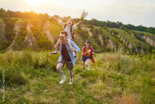 Active parents, man and woman going hiking on trails, hills with their children. Warm summer evening outdoors. Concept of leisure time, fun, nature, active lifestyle, family, travel