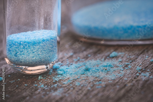 blue copper sulphate granules in glass floors - insulated close-up on wood background