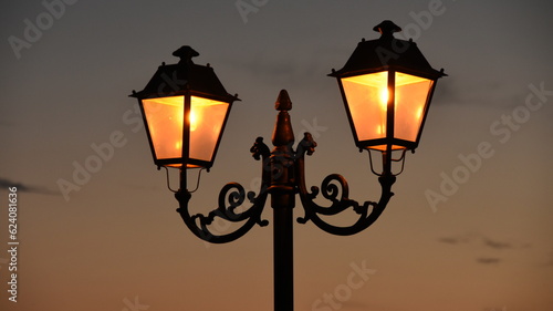 Old ornamented Street Lamp Gas light lantern retro 1800 style warm illuminated at dawn night town