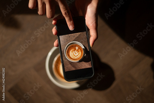 smartphone taking photograph hot cappuccino with latte art on wood background