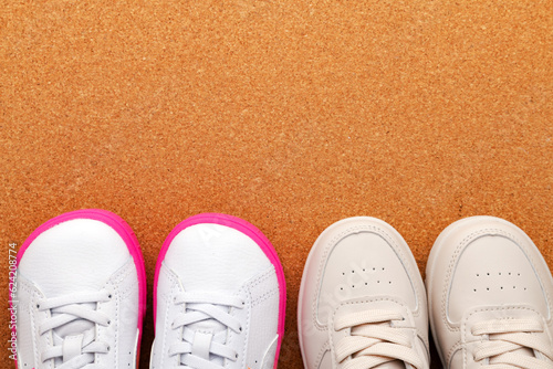 two pairs of white leather children's sneakers on a cork floor. View from above. Space for text.